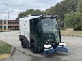 A 2019 Madvac LS175 street sweeper featuring dual side brushes and a compact design with a clear cabin and front controls