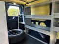 Interior view of a 2016 Ford Transit 150 showing metal shelving units and a spare tire on the floor
