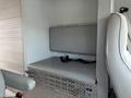 A grey interior seating area of a 1994 GMC Vandura 3500 featuring a cushioned bench with a seatbelt and a metallic storage compartment underneath