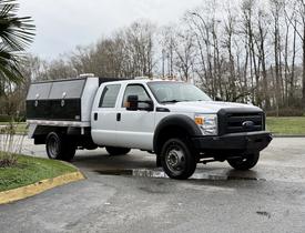 White 2016 Ford F-550 Super Duty truck with a flatbed and storage compartments on the back parked at an angle
