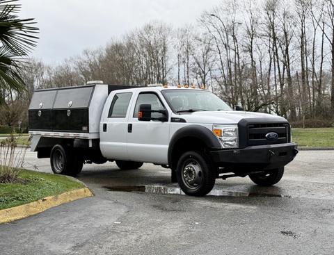 White 2016 Ford F-550 Super Duty truck with a flatbed and storage compartments on the back parked at an angle
