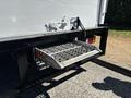 A loading ramp extended from the back of a 2022 Isuzu NRR truck featuring a textured surface for grip and a safety chain attached to the truck