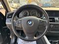 A 2013 BMW X3 steering wheel with the BMW logo and various control buttons visible along with dashboard gauges behind the wheel