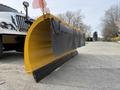 A yellow snow plow attached to a truck with a curved blade and black rubber edges