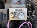 A metal control panel with a gauge labeled Ridewell Suspensions displays axle load readings and features a valve handle connected by purple hoses