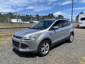 A 2015 Ford Escape in silver with a sleek design and alloy wheels parked on gravel