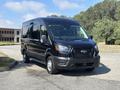 A black 2025 Ford Transit T-350 van with a modern design and front grille is parked with its headlights on
