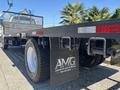A 2004 Ford F-750 flatbed truck with a black chassis and large tires featuring a sign for Abanete Motor Group attached to the rear