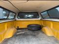 A 2014 Ford F-150 truck bed with yellow walls and a black spare tire resting on a textured floor