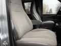 Two gray fabric seats of a 2023 GMC Savana are visible with armrests and a central console in the foreground