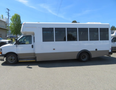 A white 2020 Chevrolet Express bus with windows on the sides and a brown lower panel is parked stationary.