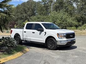A white 2021 Ford F-150 pickup truck with a black grille and wheels parked on a road