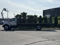 A white 2018 Ford F-750 flatbed truck stands parked with a long flatbed and large tires visible