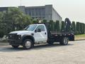 A 2009 Ford F-450 Super Duty flatbed truck with a black bed and hydraulic arm on the rear side
