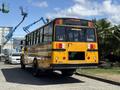 A yellow 2011 Freightliner B2 school bus with a black roof and multiple rear lights parked with construction equipment in the background