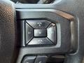 Close-up of a black steering wheel control panel featuring buttons for volume and track navigation