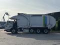A 2011 Autocar Xpeditor garbage truck with a large closed body featuring blue and green stripes on the side and three axles visible