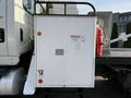 A white storage compartment on the back of a 2011 International 7500 truck with warning labels and a red fire extinguisher attached to the side