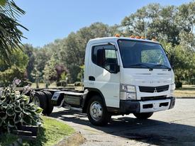 A 2015 Mitsubishi Fuso FE truck with a white cab and no cargo bed, featuring orange lights on the roof and a single row of wheels at the rear