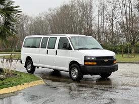 A white 2021 Chevrolet Express van with a spacious passenger compartment and black front grille standing on a wet surface