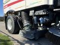 A 2012 Autocar XPERT street sweeper with large tires and a vacuum system visible underneath, featuring a metal brush attachment at the front and various hoses and connections