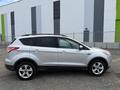 A silver 2015 Ford Escape parked on gravel with a sleek design and alloy wheels