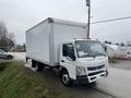 A 2012 Mitsubishi Fuso FE truck with a large white cargo box and orange lights on the roof parked on a gravel surface