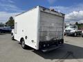 A white 2004 Ford Econoline van with a cargo box attached at the rear and a small window on the side