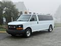 A white 2016 GMC Savana van with a black front grille and an orange light on the roof is parked on a concrete surface