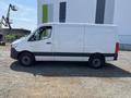 A 2022 Mercedes-Benz Sprinter van in white with a gray stripe along the bottom parked on a gravel surface displaying a side view