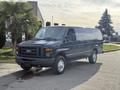 A dark blue 2011 Ford Econoline van with a boxy shape and large front grille is parked on a street. The van has no rear windows and sits on silver wheels