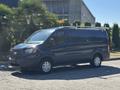 A black 2016 Ford Transit 150 van with a roof rack and amber light on top parked on a driveway