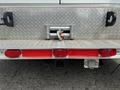 The rear of a 1994 GMC Vandura 3500 showing a metal bumper with a hitch a red reflector strip and tail lights