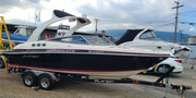 A black and white 2013 Larson 238 boat with a red stripe on a trailer with a tower for wakeboarding stands prominently in the foreground