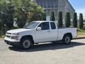 A 2011 Chevrolet Colorado pickup truck in white with a cab and open bed parked on a street with trees nearby
