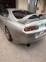 A silver 1997 Toyota Supra with a prominent rear wing and distinctive taillights parked in a driveway
