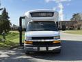A white 2017 Chevrolet Express passenger van with a large windshield and elevated front hood parked at an angle with the door open