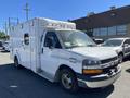 A white 2013 Chevrolet Express van with a boxy shape and emergency lights on the roof parked in a lot