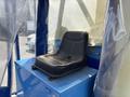 A black driver seat positioned in a blue control area with buttons and a storage compartment beneath it