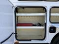 The interior of a storage compartment showing two white shelves and a red tool box with some black cords visible