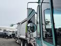 A 2020 Freightliner MT45 garbage truck with a white body and colorful logo visible on the side, featuring a large side mirror and a reflection of nearby vehicles in the mirror