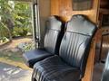 Two black vinyl seats with vertical ribbing, positioned side by side, inside a vehicle. The seats have a slightly worn look, showing signs of use over time