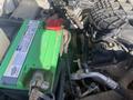 A green battery sits in the engine compartment of a 2017 Ford F-150 with various cables and components visible around it