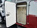A white and red truck door is open revealing an empty storage compartment with metal hooks on the interior walls
