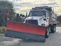 A 2013 Freightliner 114SD truck equipped with a large red snow plow attached to the front