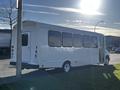 A 2014 Ford Econoline bus in white with large windows and an open side door parked near a street