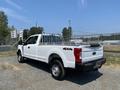 A white 2017 Ford F-250 Super Duty pickup truck with a flatbed and 4x4 markings parked in a gravel area