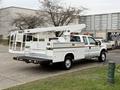 A white 2001 Ford F-350 utility truck with a cargo bed and an extended boom lift mounted on the back