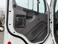 The interior door panel of a 2016 Freightliner 108SD featuring a beige armrest a black plastic handle and a transparent pocket for storage