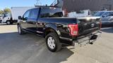 A black 2016 Ford F-150 pick-up truck parked with its rear and side visible showcasing its sleek design and alloy wheels